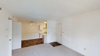 Located at 5650 Netherfield Pl in Fayetteville, North Carolina, this single-floor unit offers a straightforward and functional layout designed for comfortable everyday living. The main living area features plush carpeting that transitions into dark hardwood-style flooring, creating a clear visual distinction between the living and functional zones of the space. A ceiling fan is centrally positioned overhead, providing both lighting and air circulation throughout the open area. The textured ceiling adds a classic residential finish throughout. The kitchen is openly integrated into the living space, offering a seamless flow between cooking and living areas. It is equipped with light wood cabinetry, a sink, and essential appliances, providing all the basic necessities for meal preparation. The kitchen's open-facing design allows for easy interaction between the kitchen and the rest of the unit. The entry door is conveniently located adjacent to the kitchen area, offering direct access into the heart of the unit. The neutral, light-toned walls throughout the space create a bright and clean atmosphere, making the unit feel open and easy to personalize. Overall, this unit presents a practical and well-organized single-level living space suited for those seeking simplicity and functionality in Fayetteville, NC.
