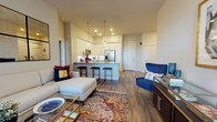 Located at 7108 E Lowry Blvd in Denver's Lowry neighborhood, this single-floor residence offers a thoughtfully designed open-concept layout with modern finishes throughout. The living area is bright and welcoming, featuring rich hardwood-style flooring, large windows that invite natural light, and a large sectional sofa paired with a decorative mirror wall accent. The kitchen is a standout feature, outfitted with crisp white shaker cabinetry extending to the ceiling, a white subway tile backsplash, stainless steel appliances including a French door refrigerator, microwave, and range, and a central island with a quartz countertop and bar seating — ideal for casual dining or entertaining. The primary bedroom is generously proportioned, offering a serene retreat with natural light from large windows, hardwood-style flooring, and tasteful décor. Additional bedrooms are equally well-appointed, each with ample natural light and neutral tones. The bathroom presents a clean, contemporary aesthetic with a glass-enclosed walk-in shower, white cabinetry, a undermount sink with quartz countertop, and light tile flooring. The overall ambiance of the space is modern, polished, and cohesive, with warm tones and quality finishes creating a comfortable and stylish living environment.