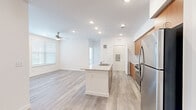 This single-floor residence features a clean, contemporary design characterized by white walls, light wood-style plank flooring, and ceiling fans throughout. The open-concept layout connects the kitchen and living area seamlessly, creating a spacious, airy atmosphere enhanced by recessed lighting and natural light from multiple windows with horizontal blinds.

The kitchen is a standout feature, equipped with warm-toned wood cabinetry, granite countertops, a white subway tile backsplash, and a full suite of stainless steel appliances including a gas range, microwave, and refrigerator. A central island with a granite top and integrated sink serves as both a functional workspace and a natural dividing point between the kitchen and the open living area.

The bedrooms are well-proportioned, each with ceiling fans, natural light from windows, and light plank flooring. The primary bathroom offers a dual-sink vanity with granite countertops, warm wood cabinetry, marble-style tile flooring, and a glass-enclosed walk-in shower. A secondary bathroom features a soaking tub with marble-style tile surround. The overall ambiance is bright, clean, and modern throughout.