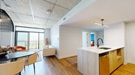 Located at 3440 Boul Saint-Elzéar O in Laval, Quebec, this well-appointed 2-bedroom, 1-bathroom unit offers a thoughtfully designed open-concept layout with a distinctly modern aesthetic. Exposed concrete ceilings run throughout the living areas, adding an industrial character that contrasts beautifully with warm hardwood flooring underfoot.

The kitchen is a standout feature, showcasing light wood and white cabinetry, a tiled hexagonal backsplash, stainless steel appliances, and a generous island with a white quartz countertop, a matte black faucet, and bar seating — ideal for both cooking and casual dining. The adjoining dining area accommodates a round table beneath a striking woven pendant light, while the living area benefits from an open, airy feel with a wall-mounted AC unit.

The primary bedroom is a comfortable retreat, featuring large windows that frame views of the surrounding neighbourhood, an exposed concrete ceiling, and an accent wall in deep teal. The second bedroom also enjoys natural light through a wide window with outdoor views. A spacious walk-in closet with built-in shelving provides excellent storage. The bathroom is clean and contemporary, with a tub-shower combo enclosed by sliding glass doors, light tile flooring, and a sage green accent wall.