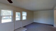This two-floor home offers a straightforward and functional layout designed for comfortable everyday living. The entryway greets visitors with tile flooring and a classic paneled front door flanked by windows that invite an abundance of natural light into the space. Just beyond the entry, the main living area transitions to wall-to-wall carpeting, creating a warm and comfortable atmosphere. The walls are finished in a clean, neutral tone throughout, providing a versatile backdrop suited to a variety of interior styles. The windows are fitted with blinds, offering practical light control while maintaining a tidy appearance. Flush with the wall, floor vents indicate a forced-air climate system to keep the home comfortable year-round. The open feel of the main level is enhanced by smooth ceilings and simple, uncluttered lines that give the space a bright and airy quality. Spanning two floors, the home provides a clear separation between living and private spaces, with the upper level offering additional room for bedrooms or auxiliary uses. Overall, the property presents a clean, move-in ready environment with timeless, understated finishes throughout.