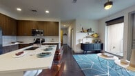 This well-designed single-floor residence offers a cohesive blend of modern aesthetics and functional living. The entryway, framed by a sleek paneled door and dark hardwood flooring, opens directly into the heart of the home. The kitchen is a standout feature, showcasing rich walnut-toned cabinetry that extends to the ceiling, a classic white subway tile backsplash, quartz countertops, and a full suite of stainless steel appliances. A generously sized kitchen island with seating provides both additional prep space and a casual dining area. The open-concept layout flows seamlessly into the living room, which features the same dark hardwood flooring and a bright, neutral palette that complements the eclectic décor. Two bedrooms offer comfortable retreats, each carpeted and filled with natural light through modern roller-shaded windows. The primary bedroom includes a walk-in closet, while both rooms feature clean, neutral walls well-suited for personalization. Two full bathrooms mirror each other in design, each appointed with large-format tile flooring, white subway-tiled tub surrounds, wood-finish vanities, and framed mirrors. The overall ambiance is modern and inviting, with consistent finishes tying each space together cohesively.