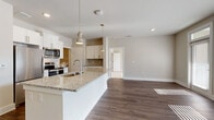 Located at Annabelle on Main in Duluth, Georgia, this single-story, 2-bedroom, 2-bathroom residence offers a thoughtfully designed open-concept layout with consistent, modern finishes throughout. Dark hardwood-style flooring runs through the main living areas, creating a cohesive aesthetic that ties the spaces together.

The kitchen serves as a central focal point, featuring a large granite-topped island with an undermount sink, white shaker cabinetry, a subway tile backsplash, stainless steel appliances, and polished pendant lighting overhead. The kitchen opens seamlessly into the dining and living areas, which are filled with natural light from multiple windows.

Both bedrooms are carpeted and include ceiling fans and windows that allow ample daylight. The primary bathroom offers a glass-enclosed walk-in shower with wood-look flooring, while the secondary bathroom features a tub-shower combination, granite vanity countertop, white cabinetry, and matching flooring. A dedicated laundry area with shelving and a washer adds everyday convenience. The overall design presents a clean, neutral palette with modern hardware and finishes throughout.
