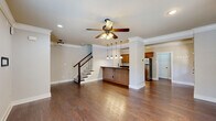 Located at 650 Dekalb St in Auburn, Alabama, this two-story home offers a thoughtfully designed layout across two floors. The main level features an open-concept living, dining, and kitchen area united by rich dark hardwood flooring and elegant crown molding. A ceiling fan with a light fixture anchors the living space, while decorative columns frame the room with classic architectural character. The kitchen is equipped with stainless steel appliances, warm wood cabinetry, dark countertops, and a beadboard-paneled breakfast bar illuminated by a row of pendant lights — ideal for casual dining or entertaining. A staircase with a dark wood banister and white balusters connects the two floors, adding a stylish focal point to the main level. Upstairs, the three bedrooms are finished with plush carpeting and ceiling fans, and each benefits from multiple windows that invite abundant natural light and outdoor views. The primary bedroom is a comfortable retreat with hardwood-style flooring. The three bathrooms feature clean, white tub-shower combinations with oil-rubbed bronze fixtures. With seven closets distributed throughout the home, storage is plentiful. A dedicated laundry room and two hallways complete the functional floor plan of this well-rounded Auburn home.