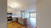 This well-designed single-floor residence offers a thoughtfully laid-out open-concept living space that seamlessly connects the kitchen, dining, and living areas. The kitchen is a standout feature, boasting granite countertops, grey shaker-style cabinetry, a subway tile backsplash, and a full suite of stainless steel appliances including a refrigerator, range, microwave, and dishwasher. A central island with a built-in sink and pendant lighting above adds both function and style, while warm hardwood-style flooring runs throughout the main living areas. The living room is bright and airy, benefiting from natural light through large windows and a set of glass doors that open to the outdoors. The bedrooms feature plush carpeting, ceiling fans, and multiple windows with blinds, allowing for ample natural light and comfortable ventilation. The bathrooms are finished with the same granite countertops found in the kitchen, grey cabinetry, and hardwood-style flooring. The primary bathroom features a double vanity and direct access to the adjoining bedroom, while a secondary bathroom includes a full tub-shower combo. Neutral tones throughout give the space a clean, modern aesthetic.
