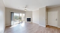 This single-floor residence is designed with a clean, contemporary aesthetic, characterized by neutral warm-grey walls, crisp white trim, and crown moulding that add a polished finish throughout the common areas. Light wood-look flooring extends across the main living spaces, enhancing the bright and airy atmosphere created by abundant natural light.

The open living area serves as the focal point of the home, anchored by a white-mantled fireplace and a ceiling fan overhead. A sliding glass door leads directly to a balcony, offering outdoor views and filling the room with sunlight. The space flows naturally into additional areas, including a well-appointed kitchen featuring white shaker-style cabinetry, light quartz countertops, a grey subway tile backsplash, and a full suite of stainless steel appliances including a dishwasher, range, and microwave.

The bedrooms are carpeted for comfort, each receiving natural light through windows with blinds. Closet space is provided via sliding and standard doors. A bathroom includes a soaking tub with tiled surround. A dedicated laundry area accommodates a full-size washer. The overall layout is functional and cohesive, with a consistently light and neutral palette maintained throughout.