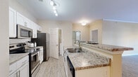 This single-floor, 3-bedroom, 2-bathroom home offers a thoughtfully designed layout with consistent, neutral tones and a blend of wood-look flooring and plush carpet throughout. The kitchen is a standout feature, showcasing white shaker cabinetry, granite-style countertops, a tile backsplash, and stainless steel appliances including a refrigerator, range, and built-in microwave. A peninsula with additional counter space connects seamlessly to the dining room via a stylish arched passageway, where a pendant light fixture and crown molding add a refined touch. The living room is bright and open, featuring wood-look tile flooring, crown molding, and windows that invite natural light. The spacious primary bedroom includes a generous walk-in closet with built-in wire shelving. The secondary bedrooms are carpeted and well-lit with natural light from windows. Both bathrooms feature white vanity cabinetry with granite-style countertops, large mirrors, and wood-look flooring. A dedicated in-unit laundry room with washer and dryer hookups provides added everyday convenience. The overall ambiance is clean, neutral, and move-in ready.
