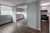 Located at 2575 Danforth Ave in Toronto's East End, this one-bedroom, one-bathroom unit offers a thoughtfully designed layout across a single floor. Wood-look flooring runs throughout, lending warmth and visual continuity to every room.

The entry hallway provides a clean transition into the living areas, with a glimpse of natural light drawing you toward the main space. The kitchen is efficiently arranged in a galley style, outfitted with stainless steel appliances including a refrigerator, electric range, and over-the-range microwave. Light wood cabinetry pairs with white upper cabinets and a light countertop, creating a bright, contemporary feel.

The bedroom is a calm, sunlit space featuring large windows that allow generous natural light. Frosted glass sliding closet doors add a sleek, modern touch, while a built-in shelving and desk unit along one wall provides practical, integrated storage and workspace.

The bathroom is finished in a clean, minimalist style with a wide quartz-topped vanity, under-mount sink, warm wood cabinetry, a large wall mirror, and a tub-shower combination — all presented in a crisp white palette.

Overall, the unit reflects a modern, functional aesthetic with consistent finishes throughout, making efficient use of its compact footprint.