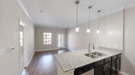Located in Round Rock, TX, this 2-bedroom, 1-bathroom single-story residence offers a thoughtfully designed layout that maximizes its comfortable footprint. The open-concept living and kitchen area serves as the heart of the home, anchored by a central island with granite countertops, a double stainless steel sink, and three pendant lights overhead. The kitchen is fully equipped with dark espresso cabinetry, a stainless steel refrigerator, range, microwave, and dishwasher, complemented by a subway tile backsplash. Rich hardwood-style flooring flows throughout the main living area, which is filled with natural light from large windows and a glass door leading to the exterior. Crown molding adds a polished finish throughout. A hallway connects the living space to the two bedrooms, both featuring plush carpet and ceiling fans. The spacious primary bedroom offers ample room and natural light. The shared full bathroom includes a granite-topped vanity with dark cabinetry, a framed mirror, tile flooring, and a tub-shower combination. A dedicated closet and additional storage round out this well-appointed residence in the heart of Round Rock.