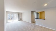 This Canterbury Apartments unit, model A1A, offers a thoughtfully designed 610 square foot living space. The single-floor layout comprises a generous 170 square foot primary bedroom, a full bathroom, a well-equipped kitchen, and a comfortable living room. 

The apartment features neutral-toned walls and plush carpeting throughout most spaces, creating a warm and inviting atmosphere. The kitchen stands out with its bright white cabinetry, modern appliances including a refrigerator and stove, and striking hardwood flooring. Ample counter space and overhead cabinets provide excellent storage and food preparation areas.

The bathroom is efficiently designed with a full-size bathtub, toilet, and vanity, complemented by white tiling and wooden flooring. Large windows in the living areas and bedroom allow for plenty of natural light, enhancing the sense of spaciousness. The living room offers direct access to an outdoor area through sliding glass doors, extending the living space.

Built-in closets in the bedroom and entryway provide additional storage solutions. The apartment's layout maximizes the use of space, creating a comfortable and functional living environment. With its blend of modern amenities and thoughtful design, this Canterbury Apartments unit offers an ideal living solution for individuals or couples seeking a well-appointed home.