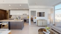Located in the heart of Downtown Los Angeles, this contemporary residence offers a sophisticated open-concept floor plan filled with abundant natural light. The living area is anchored by expansive floor-to-ceiling windows that frame striking panoramic views of the LA skyline, creating a seamless connection between interior and exterior. A private balcony extends the living space outdoors. The gourmet kitchen is outfitted with high-gloss white upper cabinetry, rich wood-grain lower cabinets, a large center island with bar seating, and stainless steel appliances — including a gas range. An in-unit stacked washer and dryer adds everyday convenience. The adjacent dining area features elegant pendant lighting and continues to benefit from the expansive window line. Two well-appointed bedrooms offer distinct character: one with a serene sage accent wall, a walk-in closet, and a circular mirror, and the other with a bold botanical wallcovering and a frosted sliding closet door. Both bathrooms are finished with large-format marble-look tile, soaking tubs with tiled surrounds, and modern vanities. The overall ambiance is clean, bright, and refined — ideal for urban living in one of LA's most vibrant neighborhoods.