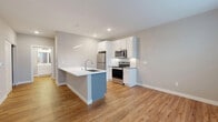 Located at 1350 Kari Court in Oconomowoc, Wisconsin, this thoughtfully designed one-bedroom, one-bathroom unit makes excellent use of its compact footprint across a single level. The open-concept kitchen and living area serves as the heart of the space, where warm hardwood flooring flows seamlessly throughout. The kitchen is well-appointed with crisp white shaker cabinetry reaching toward the ceiling, a full suite of stainless steel appliances including a refrigerator, range, and over-the-range microwave, a classic subway tile backsplash, and a peninsula island with a sleek white quartz countertop and an undermount sink — ideal for casual dining or meal prep. Recessed lighting and under-cabinet lighting enhance the bright, clean aesthetic. The living area benefits from a transom-windowed entry door that invites natural light. The bedroom offers a cozy, carpeted retreat with a generous window overlooking the surrounding neighborhood. The bathroom features a walk-in shower with sliding glass doors and hardwood-style flooring. Additional conveniences include a dedicated closet and in-unit laundry, rounding out this efficiently planned and modern living space.