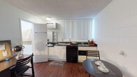 Located at 17839 Plummer St in the Northridge neighborhood of Los Angeles, this single-floor studio offers a well-organized, open-concept layout that efficiently combines living, sleeping, and dining functions within one cohesive space. Rich hardwood-style flooring runs throughout, providing a warm contrast to the bright white walls and textured ceilings.

The kitchenette is equipped with white cabinetry featuring dark countertops, a double-basin sink, a gas cooktop, a built-in dishwasher, a microwave, and a full-size refrigerator. Vertical blinds on the kitchen window allow for adjustable natural light. An open shelving unit with a mirror adds both storage and visual depth to the cooking area. A wall-mounted air conditioning unit provides climate control.

Adjacent to the kitchenette, a compact dining area accommodates a round table and chairs, making efficient use of the shared open space. The sleeping area is set apart within the same open floor plan and includes an open closet with built-in shelving, offering organized storage. A dedicated desk area makes the space functional for work or study.

The bathroom features light blue walls, wood-style flooring, and clean, simple fixtures, creating a calm and neutral atmosphere. Overall, this studio presents a practical and livable layout suitable for a single occupant seeking a self-contained space in Los Angeles.
