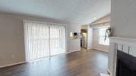 This single-floor residence offers a thoughtfully designed layout that balances open communal spaces with functional private areas. The living room is a welcoming focal point, featuring rich wood-style flooring, a textured ceiling, and a classic fireplace framed by a clean white mantel. Vaulted ceilings in this area add a sense of openness and volume. A large sliding glass door fitted with vertical blinds allows an abundance of natural light to pour in, seamlessly connecting the interior to the outdoors.

The kitchen is well-appointed with dark espresso cabinetry, granite-style countertops, and a full suite of stainless steel appliances including a refrigerator, electric range, and dishwasher. A pass-through counter with built-in shelving connects the kitchen to the living space, creating an open and communicative floor plan ideal for daily living.

Wood-style flooring carries consistently through the kitchen and living areas, while neutral-toned walls provide a clean, versatile backdrop throughout the home. The bathroom is practical and neatly finished, featuring a tub-shower combination, granite-style vanity countertop, and matching wood-style flooring. Additional rooms visible in the floor plan provide comfortable private spaces, completing a well-rounded and livable home.