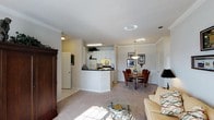 Located at 1400 Laurel Springs Dr in Durham, NC, this single-floor residence offers a well-planned open-concept layout that seamlessly connects the main living areas. The kitchen features white cabinetry, dark countertops, and a breakfast bar peninsula that opens to the rest of the living space, making it ideal for both everyday use and entertaining. Tile flooring in the kitchen transitions smoothly into plush carpeting throughout the dining and living areas. The dining area is defined by an elegant hanging pendant light fixture and is complemented by crown molding and wainscoting details along the walls, lending a refined, classic character to the space. The living room is bright and inviting, benefiting from natural light and a warm, neutral color palette. Crown molding continues throughout, adding architectural consistency and a polished feel. The layout is efficient yet comfortable, with clear sightlines across the open floor plan that enhance the sense of spaciousness. Overall, the residence combines functional design with traditional decorative details, creating a cohesive and welcoming environment throughout its single level.