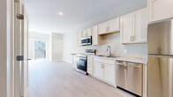 Located at 1920 Old Main St S in Cambridge, Minnesota, this single-floor unit offers a clean, modern design with a bright and cohesive aesthetic throughout. The kitchen is a standout feature, outfitted with crisp white shaker-style cabinetry, light stone countertops, and a full suite of stainless steel appliances including a range, over-the-range microwave, dishwasher, and refrigerator. The layout is efficient yet functional, with open sightlines that enhance the sense of space. Light wood-style luxury flooring runs continuously throughout the unit, complementing the neutral white and gray wall palette to create a clean, airy atmosphere. Natural light filters in through a sliding glass balcony door visible from the main living area, adding brightness to the open floor plan. The bathroom is well-appointed with a white vanity, light tile flooring, and accessibility-friendly grab bars. The bedroom area features a distinctive sliding barn door that opens to a dedicated closet, adding a stylish architectural touch. A recessed utility panel is also present in the bedroom. The unit's understated, contemporary finishes make it a well-designed and practical living space.