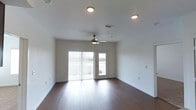 This well-appointed single-floor space offers a clean, modern aesthetic defined by a thoughtful combination of functional design and inviting finishes. The living area showcases rich, dark hardwood flooring that extends throughout, providing a warm contrast against the crisp white walls and smooth ceiling. Recessed lighting is strategically positioned overhead, complemented by a stylish ceiling fan that adds both comfort and a decorative element to the room.

Natural light plays a central role in the ambiance of this space. A large sliding glass door, dressed with vertical blinds, serves as the focal point of the main living area, flooding the interior with daylight and offering views of the surrounding outdoor landscape. An adjacent door provides additional access to the exterior, enhancing the sense of openness and connectivity to the outside.

The layout is open and versatile, allowing for a variety of furniture arrangements to suit different needs and preferences. Neutral wall tones and clean architectural lines create a blank canvas that adapts easily to various décor styles. The space is further equipped with a ceiling-mounted HVAC vent, ensuring year-round climate comfort. Overall, this space presents a bright, airy, and move-in-ready environment with a polished, contemporary feel.