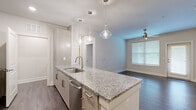 This well-appointed 2-bedroom, 2-bathroom unit in Newnan, GA offers a thoughtfully designed single-story layout. The open-concept kitchen serves as the heart of the home, anchored by a large granite-topped island with an undermount sink, stainless steel dishwasher, and pendant lighting overhead. Light-toned cabinetry pairs with stainless steel appliances, including a refrigerator, range, and microwave. Dark hardwood-style flooring extends throughout the main living areas, complementing the neutral color palette.

Both bedrooms feature plush carpeting, ceiling fans, and windows that invite natural light. The primary bedroom connects to an en-suite bathroom with a double-sink granite vanity, tile flooring, and a glass-enclosed walk-in shower with tile surround. A second full bathroom includes a tiled tub-shower combination and granite vanity. Each bedroom is served by a dedicated closet with wire shelving systems. A dedicated laundry area accommodates a full-size washer and dryer side by side. The hallway connects all rooms efficiently, contributing to the unit's functional and modern overall ambiance.