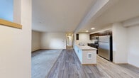 This two-bedroom, two-bathroom residence at Uptown Square in Federal Way, Washington offers a well-designed single-level layout that balances functionality with comfort. The open-concept living and kitchen area serves as the heart of the home, where light wood-style flooring flows seamlessly from the kitchen peninsula into the main living space, which transitions into plush wall-to-wall carpeting. The kitchen is outfitted with dark espresso cabinetry, stainless steel appliances including a refrigerator, range, microwave, and dishwasher, and a light-toned countertop peninsula that provides both prep space and a casual dining option. The living area is bright and open, with natural light filtering in from multiple windows. Both bedrooms are carpeted and feature neutral tones, with natural light provided by windows overlooking greenery. One bedroom includes a built-in closet with a sliding door, while another offers direct exterior door access. The bathrooms are clean and functional, with one featuring a full tub-shower combination, a single vanity with dark cabinetry, and tile-style flooring. A hallway connects the main living areas to the private bedrooms and bathrooms, creating a logical and comfortable flow throughout the residence.