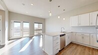 This thoughtfully designed one-bedroom, one-bathroom residence offers a modern aesthetic with quality finishes throughout. The open-concept kitchen and living area serves as the heart of the home, featuring a central island with a quartz countertop, white shaker-style cabinetry, and a full suite of stainless steel appliances including a refrigerator, range, microwave, and dishwasher. Pendant lighting above the island adds a stylish focal point, while light wood-tone flooring runs throughout the main living space, enhancing the bright, airy atmosphere. Large sliding glass doors lead to a private balcony, flooding the living area with abundant natural light and providing pleasant outdoor views. The bedroom is a comfortable retreat, finished with plush carpeting and a generously sized window that allows natural light to pour in. A dedicated closet offers practical storage. The full bathroom is clean and well-appointed, featuring white cabinetry with a dark countertop vanity, an undermount sink, a large mirror, and elegant pendant lighting. A hallway connects the private spaces with ease. Neutral warm-gray tones are used consistently throughout, lending the residence a cohesive and contemporary feel.