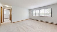 Located at 1540 E Saint Germain St in Saint Cloud, Minnesota, this single-floor unit offers a practical and straightforward layout designed for comfortable everyday living. The floor plan, visible in the 3D overview, reveals a well-organized arrangement of living spaces, a kitchen, bedroom areas, and a bathroom.

The carpeted rooms are finished in neutral tones with clean white walls, warm wood baseboards, and baseboard heating running along the perimeter. Multiple windows fitted with horizontal blinds allow natural light to flow into the space while offering views of the surrounding greenery. A wall-mounted air conditioning unit is present in the main living area, complementing the baseboard heating system for year-round climate control.

The galley-style kitchen is equipped with stainless steel appliances, including an electric range and refrigerator, set against warm oak cabinetry that lines both sides of the cooking area. A double basin sink with ample counter space adds functionality. The kitchen and bathroom feature durable wood-look vinyl flooring, providing a practical contrast to the carpeted living and sleeping areas.

The bathroom includes an oak vanity, a full tub-shower combination, and wood-look tile flooring, maintaining a consistent design aesthetic throughout. Overall, the unit presents a clean, functional living environment with consistent finishes.
