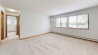 Located at 1540 E Saint Germain St in Saint Cloud, Minnesota, this single-floor unit offers a practical and straightforward layout designed for comfortable everyday living. The floor plan, visible in the 3D overview, reveals a well-organized arrangement of living spaces, a kitchen, bedroom areas, and a bathroom.

The carpeted rooms are finished in neutral tones with clean white walls, warm wood baseboards, and baseboard heating running along the perimeter. Multiple windows fitted with horizontal blinds allow natural light to flow into the space while offering views of the surrounding greenery. A wall-mounted air conditioning unit is present in the main living area, complementing the baseboard heating system for year-round climate control.

The galley-style kitchen is equipped with stainless steel appliances, including an electric range and refrigerator, set against warm oak cabinetry that lines both sides of the cooking area. A double basin sink with ample counter space adds functionality. The kitchen and bathroom feature durable wood-look vinyl flooring, providing a practical contrast to the carpeted living and sleeping areas.

The bathroom includes an oak vanity, a full tub-shower combination, and wood-look tile flooring, maintaining a consistent design aesthetic throughout. Overall, the unit presents a clean, functional living environment with consistent finishes.