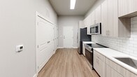 Located at 13100 Margie Ln in Raleigh, NC, this well-designed one-bedroom, one-bathroom residence offers a thoughtfully organized single-level layout. The open kitchen is a standout feature, outfitted with light wood-tone cabinetry, white quartz countertops, a classic subway tile backsplash, and stainless steel appliances including a range and over-the-range microwave. Light wood-plank flooring runs throughout the main living areas, complementing the neutral gray walls and creating a clean, contemporary aesthetic. A ceiling fan and recessed lighting provide comfortable illumination in the combined kitchen and living area, which also benefits from a window that brings in natural light. The bedroom offers plush carpeting underfoot, a dedicated closet, and a generously sized window overlooking the exterior. Its direct access to the bathroom adds a sense of privacy and convenience. The bathroom is finished with large-format subway tile in the walk-in shower, complete with a sleek sliding glass door and brushed nickel hardware. An in-unit laundry area adds everyday practicality. Throughout the space, consistent use of neutral tones, modern fixtures, and quality finishes give this residence a polished, move-in-ready feel.