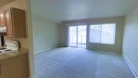 This single-floor residential space offers a clean, functional layout designed for comfortable everyday living. The living area is a standout feature, finished with plush wall-to-wall carpeting in a neutral tone that complements the light-colored walls throughout. Large sliding glass doors flood the room with natural light and open directly onto a private balcony, providing an outdoor retreat with views of the surrounding area. An adjacent window with horizontal blinds further enhances the brightness of the space, creating an airy and open atmosphere. The room's generous proportions allow for flexible furniture arrangements to suit a variety of living styles. The smooth, uniform ceiling and clean white baseboards contribute to a well-maintained and move-in-ready aesthetic. The neutral color palette throughout — from the beige carpet to the soft wall tones — creates a cohesive and calming environment. The single-floor layout ensures easy accessibility and a seamless flow between areas. Overall, this space combines practicality with a welcoming ambiance, making it well-suited for a range of occupants looking for a bright, low-maintenance living environment.