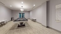 Club Torrey is a thoughtfully designed amenity facility offering residents a diverse range of social and recreational spaces, all unified by a contemporary aesthetic featuring neutral tones, recessed lighting, and polished finishes. The mail center serves as a central hub, lined with rows of individual mailboxes along both walls and accented with decorative glass art pieces and metallic spherical sculptures. A Blackbird Cold Bar station and flat-screen TV add convenience and comfort to this functional area, which also includes a seating nook with a cushioned gray sofa and a community bulletin board. The lounge area features a sleek dark wood bar-height table with modern bar stools, an artistic chandelier, and a large illuminated window bearing the Torrey Gardens signage, giving the space a club-like ambiance. Adjacent to the lounge is a dedicated billiards room with a stylish pool table, an artistic pendant light fixture, and glass double doors. A media room provides an immersive entertainment experience, anchored by a large flat-screen television set into a dramatic dark built-in wall unit with granite countertops, complemented by low-profile lounge seating. A 24/7 accessible fitness center entrance rounds out the amenity offerings, making Club Torrey a well-rounded destination for community living.