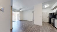 This well-appointed single-floor residence offers a clean, modern aesthetic defined by crisp white walls and durable wood-look flooring that flows seamlessly throughout every room. The open-concept living area is generously proportioned, featuring a ceiling fan, sliding glass doors dressed with vertical blinds, and an abundance of natural light that creates a bright, airy atmosphere. The space connects naturally to a galley-style kitchen, which is efficiently laid out with white shaker cabinetry, dark countertops, a stainless steel sink, and a full suite of black appliances including a refrigerator, electric range, microwave, and dishwasher. A dedicated in-unit laundry area accommodates a full-size washer and dryer side by side, adding everyday convenience. The two bedrooms are comfortably sized, each with wood-look flooring, large windows with vertical blinds that invite natural light, and ceiling fans for climate comfort. Both bathrooms maintain a clean, functional design with white tub-shower combinations and wood-look flooring. The overall ambiance of the space is light, neutral, and move-in ready, offering a practical and comfortable layout suited for everyday living.