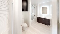 Located at 1446 Tamarind Ave in the heart of Hollywood, Los Angeles, this modern single-floor unit offers a clean, contemporary design throughout. The open-concept living and dining area is finished with warm wood-look laminate flooring, crisp white walls, and track lighting, creating a bright and inviting atmosphere. A central kitchen island with a dark countertop anchors the space, seamlessly connecting the living area to the kitchen. The kitchen is well-appointed with white upper cabinetry, dark lower cabinets, a herringbone tile backsplash, quartz countertops, a stainless steel undermount sink, and a full suite of stainless steel appliances including a gas range, microwave, refrigerator, and dishwasher. The bedroom is carpeted for comfort and features direct access to an in-unit stacked washer and dryer, adding everyday convenience. The bathroom is finished with light tile flooring and showcases a dark wood vanity with a white countertop, a backlit mirror, tall storage cabinetry, and a glass-enclosed shower-tub combination. Throughout the unit, recessed lighting, clean lines, and a neutral color palette contribute to a polished, modern aesthetic well-suited for urban living.