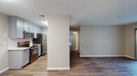 This single-floor unit offers a clean, modern aesthetic throughout, with warm wood-look flooring running continuously across all living areas. The entryway welcomes residents through a secure front door into an open layout that connects the main living spaces seamlessly.

The kitchen is a standout feature, designed in a galley style with cool-toned grey shaker cabinets, white quartz countertops, a classic subway tile backsplash, and a full suite of stainless steel appliances including a refrigerator, electric range, microwave, and dishwasher. This functional space offers ample storage and counter space for everyday use.

The open living area is bright and inviting, benefiting from natural light that pours in through a large sliding glass door fitted with vertical blinds. The slider opens directly to an outdoor patio, providing pleasant views of surrounding greenery and the broader community. An additional bedroom features a dedicated window that further enhances the natural light throughout.

The bathroom is neatly finished with a full soaking tub and shower combination, complemented by grey cabinetry consistent with the kitchen's design language. Neutral walls and wood-look flooring carry through to complete the cohesive look. The textured ceilings and crisp white trim add a polished, well-maintained character to the entire unit.