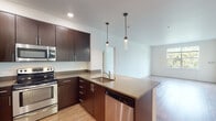 This well-appointed single-floor residence offers a thoughtfully designed open-concept layout that seamlessly connects the kitchen, dining, and living areas. The living space features warm hardwood-style flooring that reflects abundant natural light streaming through large windows, which frame picturesque views of surrounding greenery. A sliding door provides access to a private balcony, further enhancing the connection to the outdoors.

The kitchen is a standout feature, equipped with rich dark-espresso cabinetry, stainless steel appliances including a refrigerator, electric range, microwave, and dishwasher, and a neutral-toned countertop that extends to a peninsula with an undermount sink. Stylish pendant lighting above the peninsula adds a refined touch to the space.

Two well-sized bedrooms offer plush carpeting and large windows that invite natural light and treetop views, creating a calm and comfortable atmosphere. The primary bedroom benefits from a floor-to-ceiling window that maximizes its bright, airy feel.

Two full bathrooms mirror the kitchen's design aesthetic, featuring dark wood cabinetry, undermount sinks with large mirrors, hardwood-style flooring, and tub-shower combinations. Clean white walls and consistent finishes throughout the space create a cohesive, modern look.
