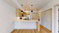 Located at 820 N State St in Bellingham, Washington, this thoughtfully designed one-bedroom, one-bathroom unit offers a clean, modern aesthetic with high-quality finishes throughout. The open-concept kitchen serves as the heart of the space, featuring warm natural wood cabinetry, a sleek white quartz peninsula with a matte black sink faucet, stainless steel appliances including a French door refrigerator, electric range, and over-the-range microwave. Light wood-grain luxury vinyl plank flooring runs throughout the main living area, while two striking black pendant lights overhead add a contemporary flair. The bedroom is carpeted and bathed in natural light from a large window overlooking the surrounding streetscape, creating a calm and comfortable retreat. A dedicated walk-in closet off the bedroom provides generous wire-rack shelving for ample storage. The bathroom is finished with light wood vanity cabinetry, matte black hardware, a white quartz countertop, and a full soaking tub and shower combo, all set on warm hardwood-style flooring. Clean white walls and recessed lighting carry a bright, airy ambiance throughout the entire unit, conveying a sense of modern urban living in the heart of Bellingham.
