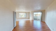 Located at 3874–3898 Darwin Dr in Fremont, CA, this single-floor unit offers a thoughtfully laid-out living space filled with natural light and practical finishes throughout. The open living and dining area is a standout feature, showcasing warm hardwood flooring, neutral-toned walls, and a textured ceiling that adds subtle character. Large windows frame views of surrounding greenery, flooding the interior with abundant natural light, while a sliding glass door provides direct access to an outdoor patio or balcony area. A step-down section in the living area creates a natural sense of spatial definition between zones. The kitchen is both functional and visually distinctive, outfitted with bold red cabinetry, granite-style laminate countertops arranged in an L-shape, a stainless steel sink, and a white gas range with overhead ventilation. Tile flooring in the kitchen provides a practical transition from the hardwood found throughout the rest of the unit. The bathroom is cleanly appointed with a combined tub and shower enclosed by sliding glass doors, a toilet, and a wood-framed vanity mirror. Additional rooms, accessible via interior doorways, offer flexible use as bedrooms or office space, each continuing the hardwood flooring and clean wall finishes. Overall, the unit presents a bright, functional living environment in a residential Fremont neighborhood.