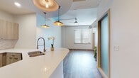 This single-floor unit presents a cohesive modern design highlighted by a mix of wood-look flooring and plush carpeting across its living spaces. The open-concept kitchen is a standout feature, equipped with stainless steel appliances including a refrigerator, electric range, and built-in microwave. Light wood-toned cabinetry lines the walls, complemented by white quartz countertops and a subtle tile backsplash. A curved kitchen island with an undermount sink anchors the space, with stylish copper pendant lights suspended above, adding a warm industrial accent.

The living area flows seamlessly from the kitchen, featuring a ceiling fan, a frosted glass sliding door, and a window fitted with blinds that allows natural light to filter in. Bedrooms offer carpeted or hardwood flooring options, with one featuring vaulted ceilings and direct access to a bathroom and walk-in closet, while another provides a window with natural light and a mirrored closet.

Two well-appointed bathrooms serve the unit. One features a glass-enclosed walk-in shower with white subway tile, while the other includes a tub-shower combination, also finished in subway tile. Both share consistent light wood vanities with white countertops, framed mirrors, and warm brass fixtures, maintaining a clean, contemporary aesthetic throughout.