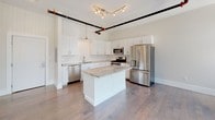 This single-floor unit blends industrial character with modern finishes throughout its well-designed layout. The kitchen serves as a standout feature, showcasing crisp white shaker cabinetry, a classic subway tile backsplash, and granite countertops that extend across a central island. A full suite of stainless steel appliances—including a gas range, built-in microwave, dishwasher, and French door refrigerator—completes the space. Overhead, exposed black pipe and track lighting add an industrial accent against the white ceiling.

The main living area is generously proportioned, featuring rich hardwood flooring that reflects abundant natural light streaming through a wide bank of floor-to-ceiling windows dressed with vertical blinds. Exposed HVAC ductwork runs along the ceiling, reinforcing the loft-inspired character of the space.

The bedrooms are carpeted for comfort, with one room offering dual closets and built-in shelving, while another benefits from large windows with outdoor views. Both bathrooms are finished with light ceramic tile flooring, granite-topped vanities, and clean white fixtures. One bathroom includes a towel warming rack and bathtub, adding a refined touch to the overall design.