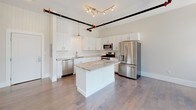 This single-floor unit blends industrial character with modern finishes throughout its well-designed layout. The kitchen serves as a standout feature, showcasing crisp white shaker cabinetry, a classic subway tile backsplash, and granite countertops that extend across a central island. A full suite of stainless steel appliances—including a gas range, built-in microwave, dishwasher, and French door refrigerator—completes the space. Overhead, exposed black pipe and track lighting add an industrial accent against the white ceiling.

The main living area is generously proportioned, featuring rich hardwood flooring that reflects abundant natural light streaming through a wide bank of floor-to-ceiling windows dressed with vertical blinds. Exposed HVAC ductwork runs along the ceiling, reinforcing the loft-inspired character of the space.

The bedrooms are carpeted for comfort, with one room offering dual closets and built-in shelving, while another benefits from large windows with outdoor views. Both bathrooms are finished with light ceramic tile flooring, granite-topped vanities, and clean white fixtures. One bathroom includes a towel warming rack and bathtub, adding a refined touch to the overall design.