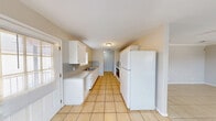 This single-floor residence offers a thoughtfully organized layout encompassing a combined kitchen and living room, one bedroom, one bathroom, and a closet. Light-toned ceramic tile flooring runs consistently throughout the home, giving the space a clean, cohesive look that is both practical and easy to maintain.

The kitchen features white cabinetry with arched detailing, a double-basin stainless steel sink, speckled gray countertops, a tile backsplash, and full-size white appliances including a refrigerator and range. Natural light filters in through window blinds, brightening the galley-style workspace.

The living room is open and airy, finished with crown molding, neutral gray walls, and a ceiling fan with a light fixture. A window with blinds allows natural light to flow in, while the clean lines and neutral palette create a versatile backdrop for any furnishing style.

The bedroom is a comfortable, well-proportioned space, also featuring a ceiling fan, a window with blinds, and the same tile flooring, ensuring a uniform feel throughout the home.

The bathroom is neatly appointed with a single-sink vanity with speckled countertop, white upper cabinetry for storage, a full tub-shower combo, and tile flooring. The overall ambiance of the home is bright, clean, and functional.