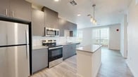 Located at 7501 Jefferson St NE in Albuquerque, New Mexico, this well-appointed one-bedroom, one-bathroom unit offers a thoughtfully designed open-concept layout finished with light wood-tone flooring throughout. The contemporary kitchen serves as the heart of the space, showcasing two-tone cabinetry in grey and warm brown, a white subway tile backsplash, light quartz countertops, a central island with pendant lighting, and a full suite of stainless steel appliances including a refrigerator, range, microwave, and dishwasher. The kitchen flows seamlessly into the living area, which is bathed in natural light through large windows and a sliding glass door fitted with vertical blinds, offering outdoor views. The bedroom is a comfortable, well-lit room featuring a large window with exterior views and ample closet storage, supported by two dedicated closets. The bathroom and remaining spaces maintain the same clean, modern aesthetic with neutral tones and crisp white walls. The overall ambiance is bright, clean, and contemporary, making efficient use of the available floor area with a practical and stylish design throughout.