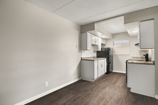 Cocina contemporánea con elegantes gabinetes blancos, electrodomésticos modernos y una encimera elegante, todo ello sobre un elegante suelo de madera. - Alderman Park Apartments