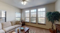 This single-floor residence offers a thoughtfully designed open layout that seamlessly connects its primary living areas. The living room serves as a central gathering space, highlighted by tall windows with transom panels that flood the room with natural light and provide views of the surrounding exterior. A ceiling fan overhead and plush carpeting underfoot contribute to the room's comfortable, relaxed atmosphere.

The kitchen is well-equipped, featuring rich dark cabinetry, granite countertops, black appliances, and a peninsula with a sink that opens toward the main living area — ideal for both cooking and entertaining. A dedicated dining nook with tile flooring sits nearby, offering an intimate setting for meals.

The primary bedroom is generously sized with soft carpeting, a ceiling fan, and French doors that allow additional natural light into the space. The accompanying bathroom includes tile flooring, a dark wood vanity with a granite-topped sink, and convenient accessibility features including a grab bar. An adjacent walk-in closet adds practical storage.

A secondary room provides flexible use as a guest bedroom or sitting area, with carpeted floors and a bright window. The open-concept flow and neutral palette throughout create a cohesive, welcoming environment.
