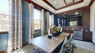 Located at 2200 N Loop 336 W in Conroe, Texas, this sophisticated conference and media room offers a refined, professional environment designed for productive meetings and gatherings. The single-floor space is thoughtfully appointed with distinctive architectural details, including a coffered ceiling with crisp white trim and rich dark wood moldings that frame the room with elegance.

Bold teal-blue walls create a striking backdrop, complemented by tall windows dressed with bold, patterned drapes that allow generous natural light to pour in while offering views of the surrounding exterior. A large, light-wood conference table anchors the room, surrounded by ergonomic rolling chairs and accented with tasteful decorative centerpieces including sculptural and botanical elements.

Underfoot, a geometric-patterned carpet in blue and gray tones adds visual depth and texture. The built-in kitchenette area features rich dark wood cabinetry, a polished dark granite countertop, a stainless steel under-counter refrigerator, and wall-mounted flat-screen monitors — making this space ideal for presentations and collaborative work sessions.

Entry is provided through handsome dark wood French doors with glass panels, adding a classic touch. A wall-mounted artwork piece and subtle signage complete the polished, well-curated ambiance of this functional and visually impressive meeting space.