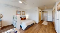Located at 201 NE 103rd St, Unit 412 in Seattle, WA, this studio unit offers a thoughtfully designed open-concept layout that maximizes every square foot of its single-floor footprint. Warm hardwood-style flooring runs throughout the space, lending a cohesive and inviting feel from entry to living area.

The kitchen is efficiently arranged along one wall and features light maple cabinetry extending to the ceiling for ample storage, white appliances including a refrigerator, electric range, dishwasher, and a single-basin sink. Recessed lighting illuminates the workspace, and a built-in range hood adds practical functionality. The kitchen flows seamlessly into a dining nook and a comfortable living area, with a window providing natural light and a connection to the outdoors.

A white modular shelving unit serves as a subtle room divider between the living and sleeping areas, creating a sense of defined zones within the open plan. The sleeping area accommodates a full-sized bed and benefits from a ceiling fan, recessed lighting, and wall-mounted art. A wood-panel entry door adds a warm architectural accent.

The bathroom is clean and functional, featuring a vanity with light maple cabinetry, a white countertop with an undermount sink, a large mirror, and a shower/tub combination. Neutral tones throughout create a calm, practical atmosphere well-suited to everyday living.