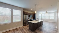 This single-floor unit is designed with a contemporary aesthetic and a functional open-concept layout. The kitchen serves as the centerpiece, showcasing dark espresso-toned cabinetry with sleek bar-pull hardware, light quartz countertops, and a full suite of stainless steel appliances including a French door refrigerator, electric range, and built-in microwave. A generously sized kitchen island with an integrated sink and pendant lighting above provides additional prep space and casual seating potential. Subway tile backsplash adds a classic yet modern touch to the cooking area.

Wood-look plank flooring extends through the open living and kitchen areas, creating a warm, cohesive feel. Multiple windows fitted with horizontal blinds allow ample natural light to fill the space. The living area flows seamlessly from the kitchen, providing a bright and airy atmosphere.

The bedrooms feature plush carpeting, ceiling fans, and natural light from multiple windows. At least one bedroom includes access to a walk-in closet with built-in shelving. The bathroom is finished with a dark vanity, white quartz countertop, dual sinks, and wood-look tile flooring, maintaining consistency with the home's modern design language throughout.