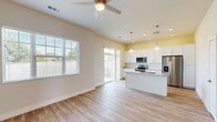 This single-story, 2-bedroom, 2-bathroom home offers a thoughtfully designed open-concept layout finished with light wood-style flooring throughout. The combined kitchen and living area forms the heart of the home, filled with natural light from large windows and a sliding glass door that opens to the backyard. The kitchen is a standout feature, showcasing white shaker cabinets, granite countertops, a center island with an undermount sink, stainless steel appliances including a French door refrigerator and electric range, and elegant globe pendant lighting overhead. A ceiling fan anchors the living area, enhancing airflow and comfort. The primary bedroom is a comfortable retreat featuring dual closets and direct access to its own en-suite bathroom, which includes a glass-enclosed walk-in shower, granite vanity, and white cabinetry. The second bedroom benefits from multiple windows that invite natural light and outdoor views. Additional storage is provided through a dedicated walk-in closet with built-in shelving and hanging rods. Three hallways connect the rooms efficiently throughout the home. The exterior features a generously sized, fenced backyard with a lawn area, offering excellent outdoor living potential.