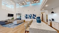 Located at 833 E Magnolia Dr in Tallahassee, FL, this single-story space is designed with a contemporary aesthetic that prioritizes openness, natural light, and refined finishes throughout. The architecture is immediately distinguished by dramatically tall ceilings with coffered detailing and strategically placed clerestory windows that flood the interior with abundant natural light, creating an airy, expansive atmosphere.

The main living area is generously proportioned, featuring light wood-toned flooring that flows seamlessly throughout the space. Multiple distinct seating arrangements are thoughtfully curated, including velvet blue sofas paired with marble-top coffee tables and patterned area rugs in coordinating blue tones. Large-scale abstract artwork adorns the crisp white walls, contributing to the polished, gallery-like ambiance.

A long granite-topped bar with upholstered seating anchors the central gathering zone, while ceiling fans with integrated lighting provide both function and style overhead. The kitchenette area includes white cabinetry, granite countertops, stainless steel appliances, and pendant lighting. Adjacent to the main area, a glass-walled fitness room offers visibility and accessibility. Large exterior-facing doors and windows throughout ensure strong connectivity to the outdoors.
