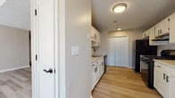 This single-floor residence offers a well-organized layout designed for comfortable everyday living. The living area is a standout space, featuring soaring vaulted ceilings with a textured finish and light hardwood-style flooring that extends throughout the main areas, creating an open and airy atmosphere. A large arched window and additional standard windows allow abundant natural light to fill the space.

The galley-style kitchen is efficiently designed with white cabinetry accented by matte black hardware, light-toned countertops, and black appliances including a gas range with overhead ventilation. A built-in sink, dishwasher, and a full-size refrigerator complete the setup, while light hardwood-style flooring continues underfoot. A pantry closet at the end of the kitchen provides additional storage.

The bedrooms are finished with plush carpeting and feature windows with exterior views, ceiling fans for climate control, and generous closet space. The bathrooms are clean and functional, each equipped with a full tub and shower combo, wood-style flooring, and matte black fixtures and towel bars throughout, maintaining a cohesive design aesthetic across the entire residence.