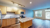 Located at 9400 Lexington Avenue North in Circle Pines, MN, this one-bedroom, one-bathroom unit offers a well-organized single-floor layout designed for comfortable everyday living. Rich hardwood-style flooring flows consistently throughout the space, creating a warm and cohesive aesthetic.

The combined kitchen and living room serves as the heart of the unit. The kitchen is well-appointed with light maple cabinetry, granite countertops, a central island for additional prep space, stainless steel appliances including a refrigerator, range, microwave, and dishwasher, and track lighting overhead. The living area benefits from large windows fitted with vertical blinds, allowing generous natural light and views of the surrounding greenery.

The bedroom is a comfortable and well-proportioned space, featuring a large window with outdoor views, adding brightness and a connection to the exterior landscape. A closet provides practical storage, while a hallway connects the rooms efficiently.

The bathroom features a full tub-shower combination, a wood-toned vanity with a white countertop, and clean white finishes throughout. An entry door with a transom window in the living area adds an additional source of natural light, completing this thoughtfully arranged and move-in-ready unit.