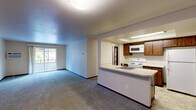 This two-bedroom unit in Coeur d'Alene, Idaho offers a functional and comfortable single-floor layout. The open-concept living and kitchen area forms the heart of the home, where a peninsula-style counter separates the two spaces while maintaining a connected, airy feel. The living room is generously sized, featuring plush carpeting, a textured ceiling, and a sliding glass door that opens to a private balcony, filling the space with natural light and views of surrounding greenery.

The kitchen is well-equipped with warm wood cabinetry, a white electric range, built-in microwave, full-size refrigerator, and tile flooring. A skylight above the kitchen adds additional brightness to the cooking area.

The spacious primary bedroom features sliding glass door access to an outdoor balcony, carpet flooring, a wall-mounted air conditioning unit, and a dedicated closet. The second bedroom is also carpeted and includes its own closet with built-in shelving, providing practical storage solutions. Both bedrooms are connected via a central hallway with dark wood-trimmed doors that add a classic touch throughout.

Baseboard heating is present in multiple rooms, ensuring comfort year-round. The overall layout is efficient and well-organized, making this unit a solid residential option in the Coeur d'Alene area.